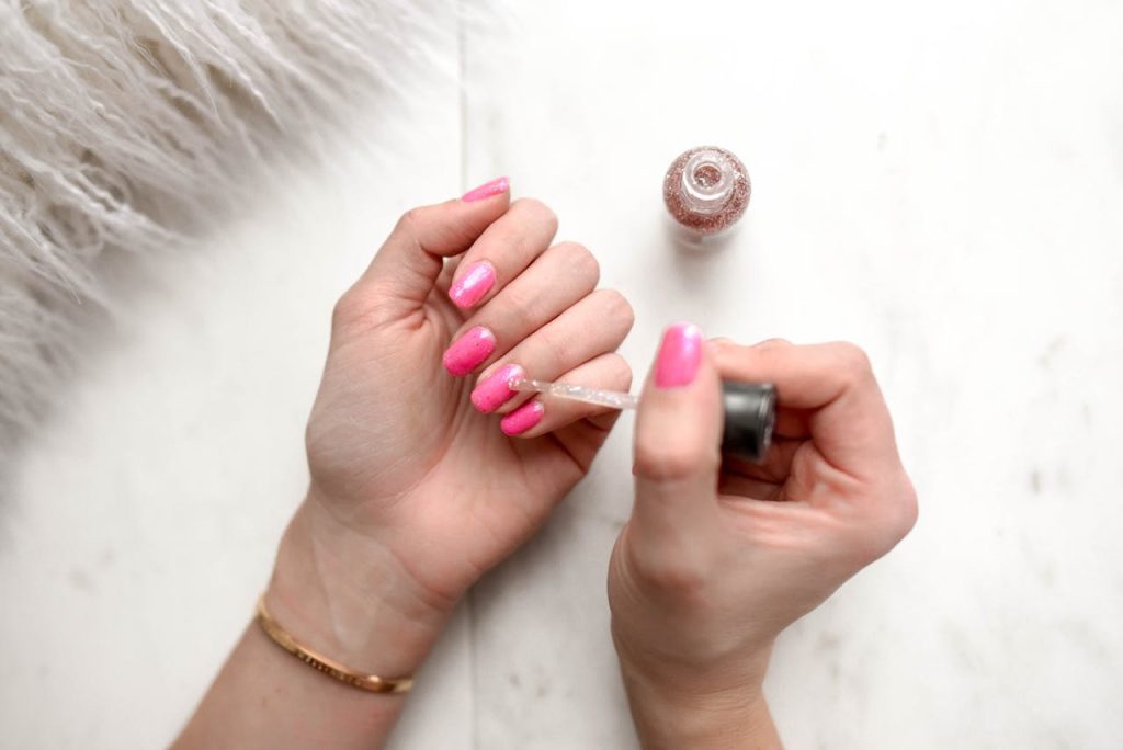 pexels-photo-973405 Close-up of a woman applying glitter nail polish to manicured pink fingernails.
